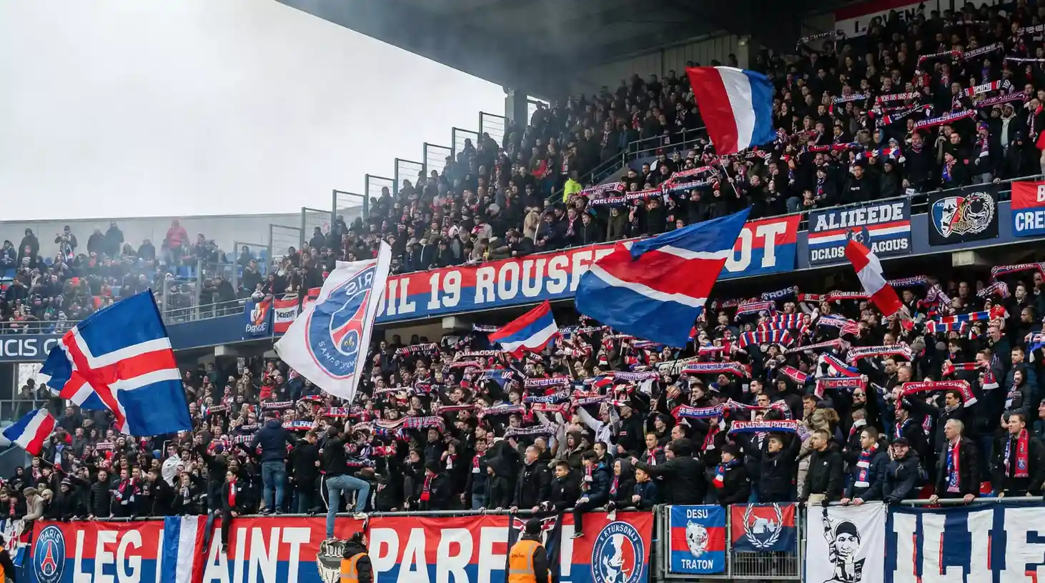 Aficionados de fútbol francés con bufandas y banderas en grada de estadio